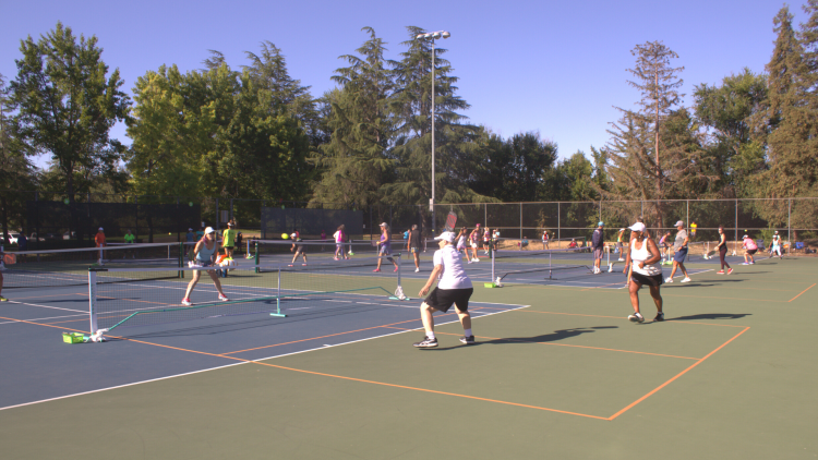 People playing pickleball outdoors on a green and blue court