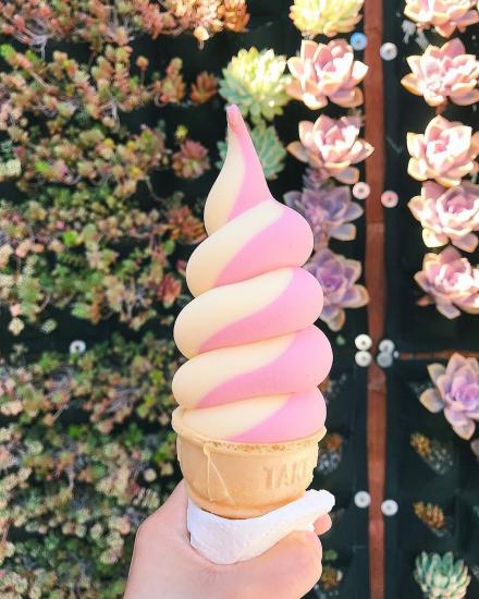 A hand holding pink and white striped soft serve ice cream on a cone