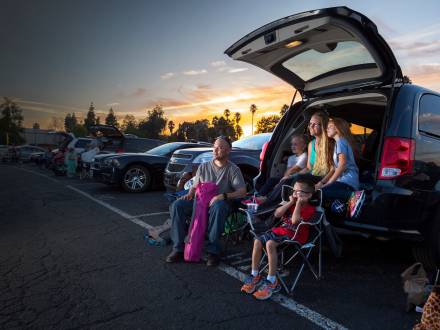 family sitting by car at drive-in
