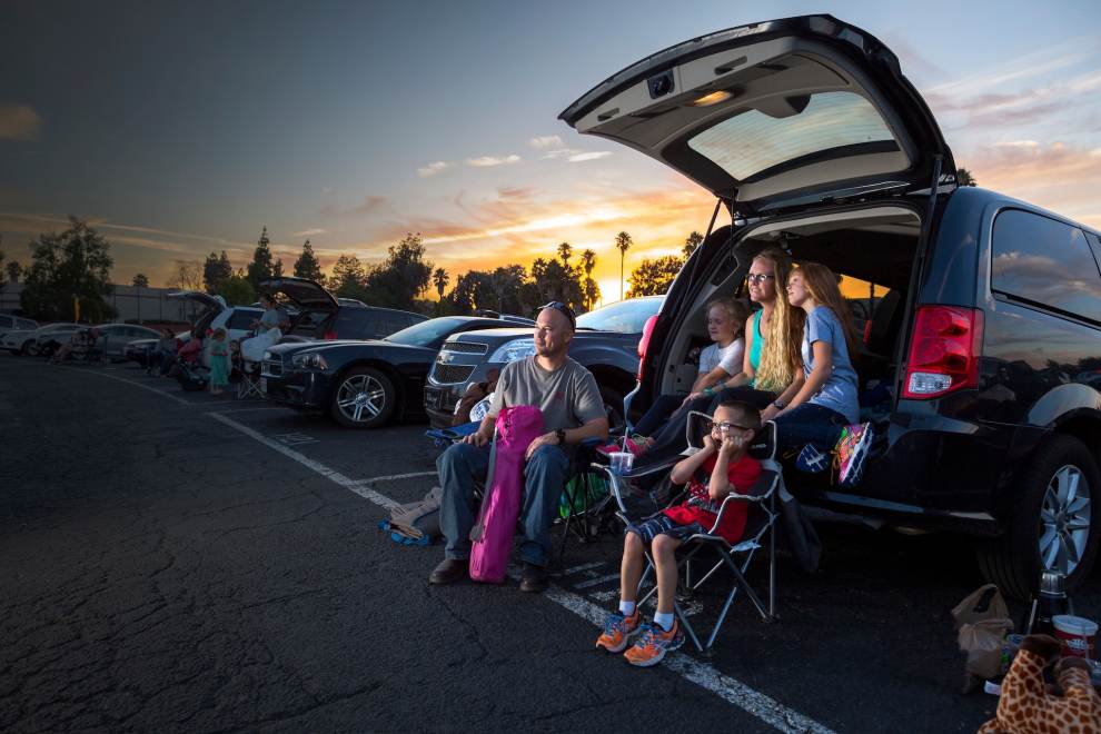 family sitting by car at drive-in