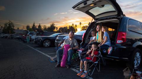 family sitting by car at drive-in