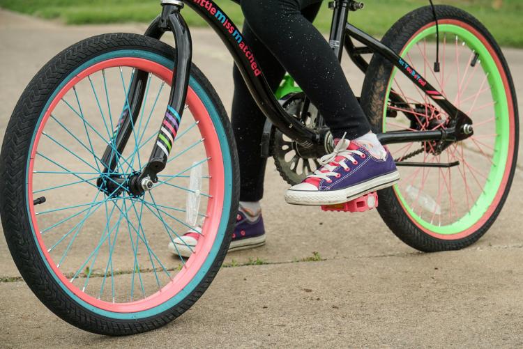 A child with a foot on their bike pedal is stopped on the sidewalk 