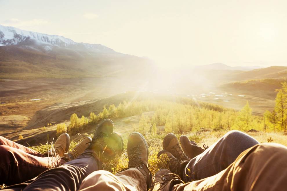 Group of hikers sitting on a hilltop with the sun rising between mountains in the distance