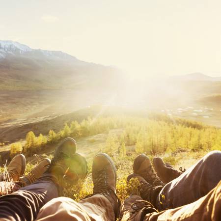 Group of hikers sitting on a hilltop with the sun rising between mountains in the distance