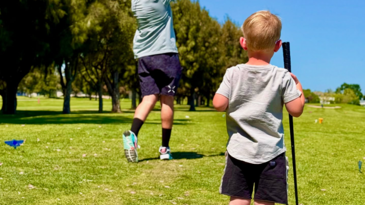 A little boy watching his dad swing a golf club